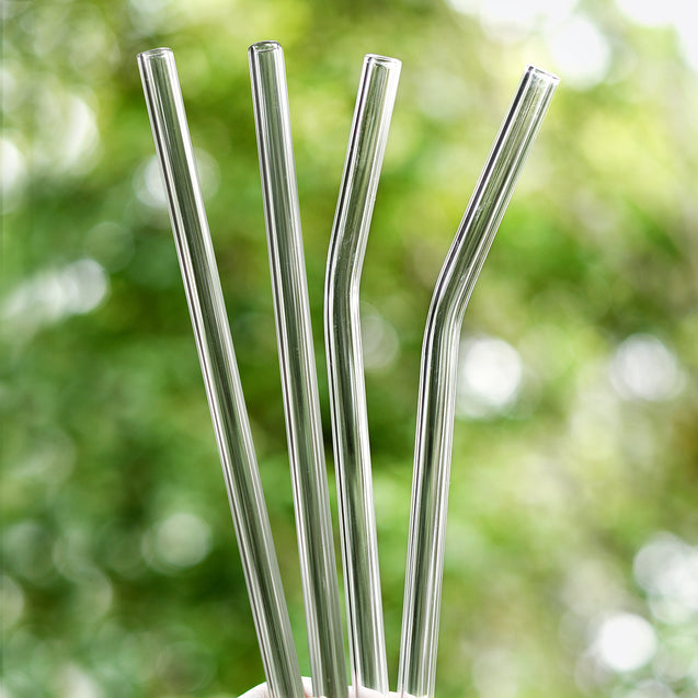 holding 2 straight and 2 bendy glass straws outdoors